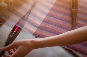 mujer trabajando en una máquina de tejer para tejer tela hecha a mano. tejido textil. tejido en telar manual tradicional sobre hebras de algodón. producción textil o de telas en tailandia. cultura asiática. foto
