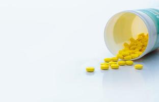 Yellow tablets pills spread out of drug bottle. Tablets pills with bottle on white table. Drug production in pharmaceutical industry concept. Healthcare and medicine background. Medication use. photo