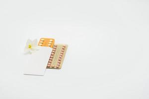 Birth control pills or contraceptive pill with paper case and white flower on white background. Family planning concept. Hormone replacement therapy. Hormonal acne treatment with anti-androgenic pill. photo