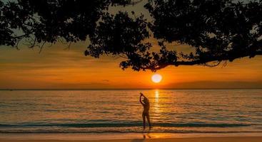 silueta vista trasera de una mujer sexy viendo la hermosa puesta de sol en la playa del paraíso tropical. niña feliz usar bikini y sombrero de paja relajantes vacaciones de verano. viajes de vacaciones vibras de verano. vida pacifica. foto