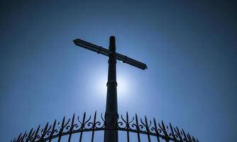 Stainless steel cross and fence on blue sky and sun light background. Crucifix of Jesus Christ. God light and forgiveness concept. Crosses, Christian symbols. Belief in god. Symbol of faith. Easter. photo
