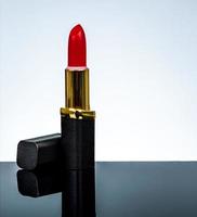 Red matte lipstick in gold and black tube package put on dark table isolated on white background in studio. Red lipstick with open cap. Makeup beauty cosmetic for confident fashion women. photo