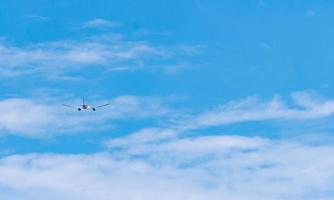 Commercial airline flying on blue sky and white fluffy clouds. Airplane flying on sunny day. Rear view of international flight passenger plane. Summer vacation travel abroad. Air transportation. photo