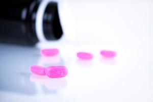 Pink tablet pills on blurred background of opened cap amber bottle on white background. Expired medicine. Drug degradation concept. Quality control of pharmaceutical industry. Tablet picking. photo