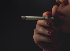 Woman with red nail is smoking cigarette on dark background. Quit smoking concept. Bad habit in woman can cause aging and lung cancer. Stressed woman. Nicotine addicted. 31 May World no tobacco day.