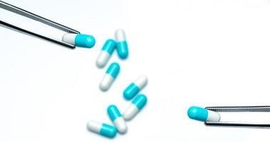 Forceps pick white-blue capsule from group of capsule pills. Drugs choose. Antibiotic drug selection. Antibiotic drug resistance concept. QA and QC in pharmaceutical factory concept. Drugs of choice. photo