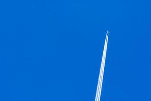 Airplane with white condensation tracks. Jet plane on blue sky and white clouds with vapor trail. Travel by airplane concept. Trails of exhaust gas from airplane engine. Aircraft with white stripes. photo