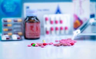 Pile of colorful tablets and capsules pills on blurred drug tray, bottle, and capsule in blister pack. Pharmacy shop background. Healthcare and drug use for treatment illness. Pharmaceutical industry. photo