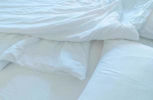 White comfort bed and soft pillow in modern bedroom. White linen blanket in hotel bedroom. Closeup detail of messy white blanket after waking up in morning. Comfortable bed with soft white duvet. photo