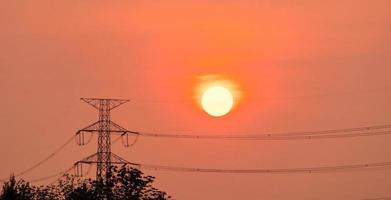 poste eléctrico de alto voltaje y líneas de transmisión al atardecer con cielo y nubes naranjas y rojas. arquitectura. torres de electricidad de silueta durante la puesta de sol. poder y energía. conservación de energía. foto