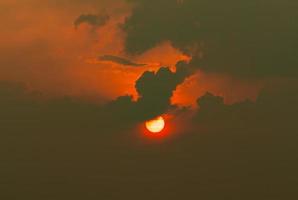 Red sun in dark clouds. Summer sunset. Fiery sun in the evening. Nature background. Dramatic dark and red sky with sunset . Heat weather. Heaven concept. Background for peaceful and tranquil concept. photo