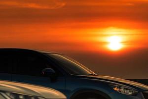Side view of blue SUV car with sport and modern design parked on concrete road at sunset. Hybrid and electric car technology. Road trip. Automotive industry. Car parking lot with beautiful sunset. photo