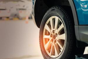 Selective focus on blue SUV car rear wheel on blurred background. Car with new high performance tire parked at garage workshop after change tyre and maintenance. Check up tire before travel concept. photo