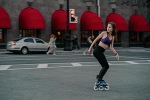 Full length shot of active slim young woman dressed in sportsclothes rides on rollers to strengthen arms and legs muscles improves balance agility and coordination has good mood burns calories photo