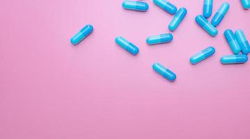 Top view capsule pills on pink background. Prescription drugs. Blue capsule pills. Pharmaceutical industry. Medicament and pharmacology. Drug development and new drug research. Capsule pills industry. photo