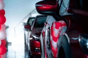 Selective focus red SUV car parked in modern showroom. Car dealership concept. Automotive industry. Auto leasing business. Luxury showroom decor with red and white ballons for promotions and events. photo