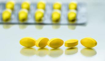 Macro shot detail of yellow oval tablet pills on white background with blister packs as background photo