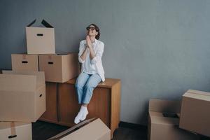 Happy young european woman purchases real estate. Thanks god. Girl is sitting on boxes and dreaming. photo