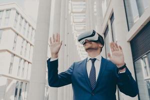 Young modern businessman in VR goggles on head working in augmented reality world and smiling photo