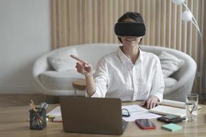 Female office worker in vr headset or virtual reality goggles touching objects in cyberspace photo