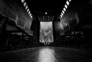 Perspective view in church. A few people sit on wooden bench with many of empty bench in church on Sunday. Black and white scene of wooden building interior with ceiling lamp. Europe architecture. photo