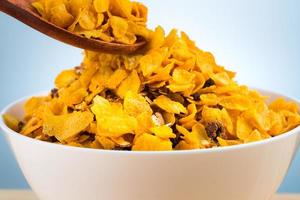 A white bowl of cereal with wood spoon on brown wooden table with copy space. Breakfast for children before go to school in the morning. Yellow cornflakes. photo