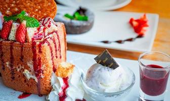 Honey toast topping with strawberries, a side of whipped cream, vanilla ice cream. Bread toast on white dish on blurred background of chocolate lava cake. Summer desserts. High calories food. photo