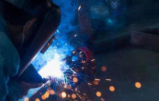Welder welding metal with argon arc welding machine and has welding sparks. A man wears a welding mask. Safety in industrial workplace. Welder working with safety. Steel industry technology.