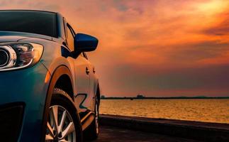 Blue compact SUV car with sport and modern design parked on concrete road by the sea at sunset. Environmentally friendly technology. Business success concept. photo