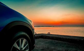 camión suv compacto azul con diseño deportivo y moderno estacionado en una carretera de hormigón junto al mar al atardecer. tecnología respetuosa con el medio ambiente. concepto de éxito empresarial. foto