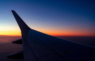 Wing of plane with sunrise skyline. Airplane flying in the sky. Scenic view from airplane window. Commercial airline flight. Plane wing above clouds. International flight. Travel abroad after covid-19 photo