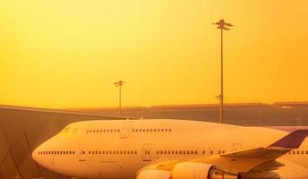 avión comercial estacionado en el aeropuerto. crisis empresarial mundial de la aviación por el coronavirus. vuelo de vacaciones de viaje fallido. transporte aéreo. avión estacionado en el aeropuerto con cielo naranja del amanecer. foto