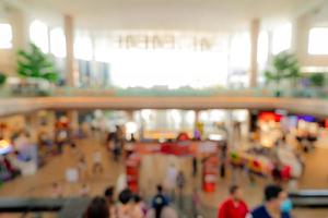 Blur crowded people inside shopping mall. Defocus retail shop in shopping center with bokeh background. People walking and on escalator at first floor of building. Shopping mall interior. Retail store photo