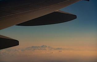 Wing of plane over blurred mountain cover with white snow. Airplane flying. Scenic view from airplane window. Commercial airline flight. Plane wing. Flight mechanics concept. International flight. photo