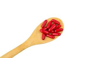 Red vitamins and supplements capsule on wooden spoon isolated on white background with clipping path and copy space for text. Use for advertising design on health content topics photo