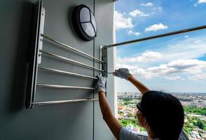 Asian woman use screwdriver screwing screw into the apartment wall for install clothes line. Thai woman wears safety glasses and holding screwdrivers. Woman working home improvement with DIY concept. photo