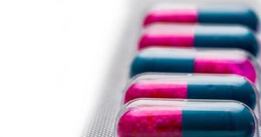 enfoque selectivo de cápsula azul y rosa con gránulos en pastillas laterales. pastillas en blister sobre fondo blanco. forma de dosificación farmacéutica y envase. itraconazol 100 mg medicamento antifúngico. foto