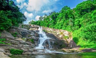 Beautiful waterfall at the mountain with blue sky and white cumulus clouds. Waterfall in tropical green tree forest. Waterfall is flowing in jungle. Nature abstract background. Granite rock mountain. photo