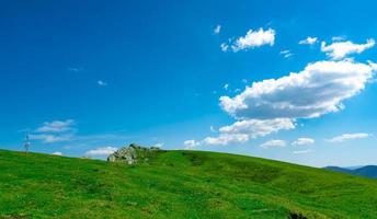 Landscape of green grass and rock hill in spring with beautiful blue sky and white clouds. Countryside or rural view. Nature background in sunny day. Fresh air environment. Stone on the mountain. photo