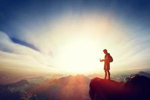 hombre conectándose con su teléfono inteligente en la cima de la montaña. comunicación foto