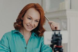 Close up shot of happy redhead woman records video on webcam, talks to subscribers, has personal blog, gives advice, makes live broadcast or fims webinar. Online teacher records vlog teaches languages photo
