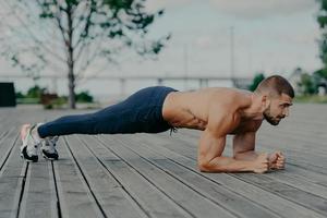 atleta masculino motivado hace ejercicio abdominal, disfruta del entrenamiento de culturismo al aire libre y se para en tablón. hombre adulto europeo musculoso fuerte tiene entrenamiento de fitness. personas y concepto de estilo de vida saludable foto