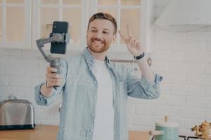 Handsome smiling young brunete man with stubble making selfie in kitchen photo