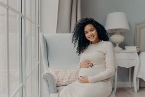 Positive pregnant woman touching gently her belly and smiling photo