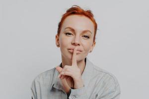 Caucasian female showing shh shush gesture, isolated on grey studio background photo