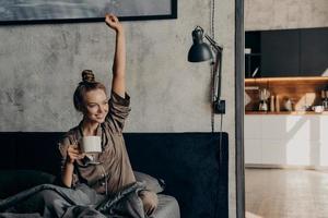Attractive young happy female having morning coffee in bed photo
