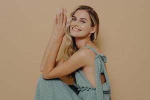 Beautiful elegant blond woman in evening dress sitting squatted on chair sideways with folded palms photo