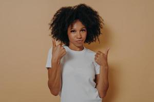 Confident young african woman showing thumbs up with both hands while standing on beige background photo