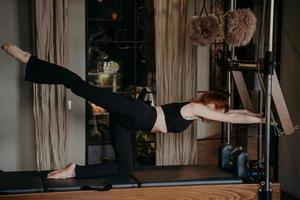 Young athletic woman exercising and stretching leg on pilates reformer photo