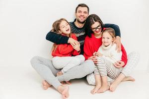 concepto de relación familiar. linda y alegre niña pequeña diviértete y disfruta del tiempo libre con sus padres. padre varón feliz abraza a su esposa e hijas, se siente encantado, aislado en blanco foto